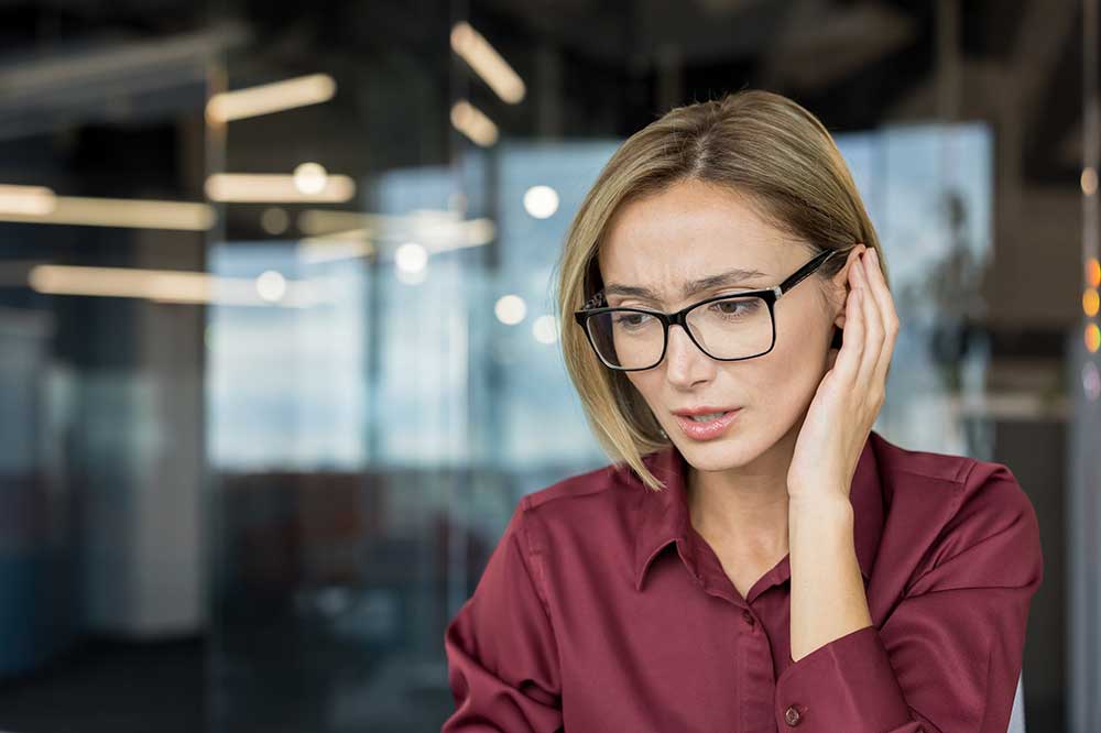 Woman in glasses touching her ear with a worried look, as when hearing seems uneven, from Clear Choice Hearing Aid, Inc. in Southern California