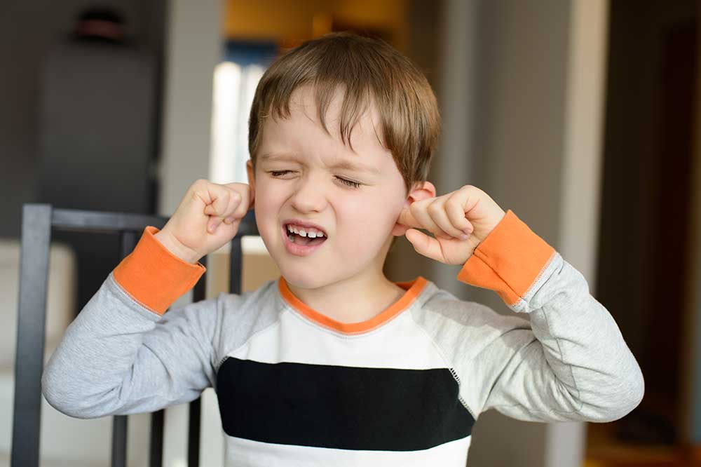 Boy pressing his fingers into both ears over a clogged ear feeling, from Clear Choice Hearing Aid, Inc. in Orange, San Diego and Riverside Counties